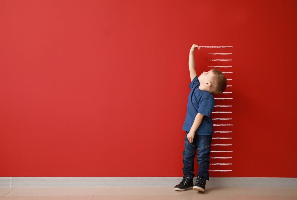 Little boy measuring height near color wall